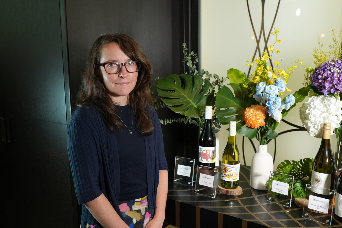 Erin Pooley 於 Little Frances 酒款展示桌旁微笑入鏡,桌上可見 11th House Sorella 等代表酒款。